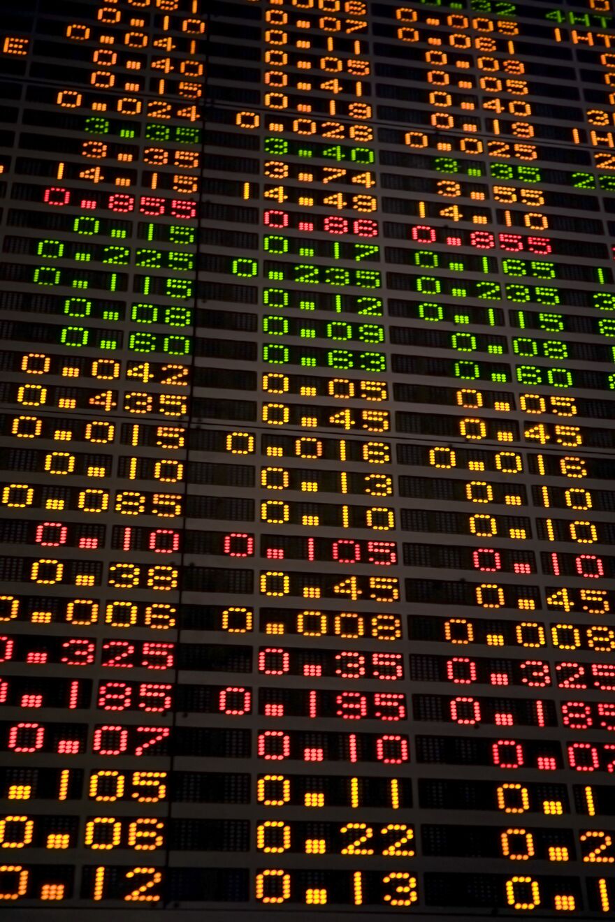 A close-up LED ticker board showing live stock prices in red, green and amber.